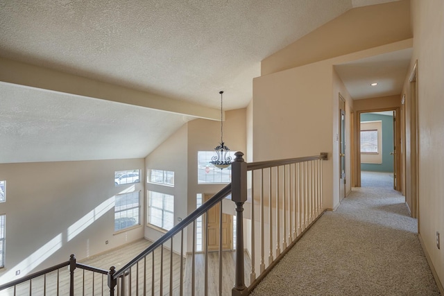 hall featuring a healthy amount of sunlight, an upstairs landing, a notable chandelier, and lofted ceiling