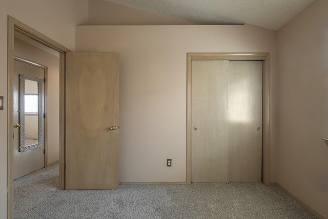 unfurnished bedroom featuring lofted ceiling, a closet, carpet flooring, and a textured ceiling