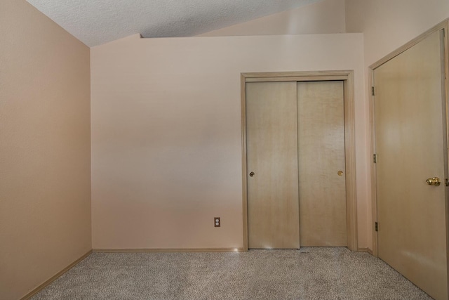 unfurnished bedroom with lofted ceiling, a closet, a textured ceiling, and carpet flooring