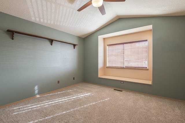 carpeted empty room featuring ceiling fan, a textured ceiling, visible vents, baseboards, and vaulted ceiling