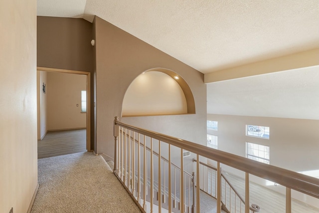 hall with carpet floors, vaulted ceiling, and a textured ceiling