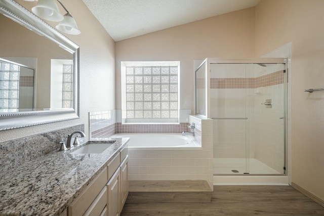 bathroom with wood finished floors, vanity, vaulted ceiling, a bath, and a stall shower