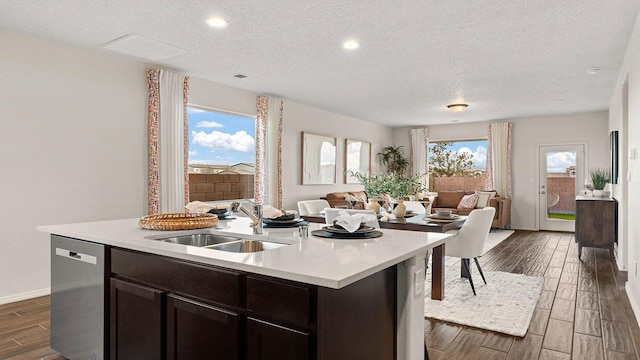 kitchen with light countertops, wood finish floors, a sink, open floor plan, and stainless steel dishwasher