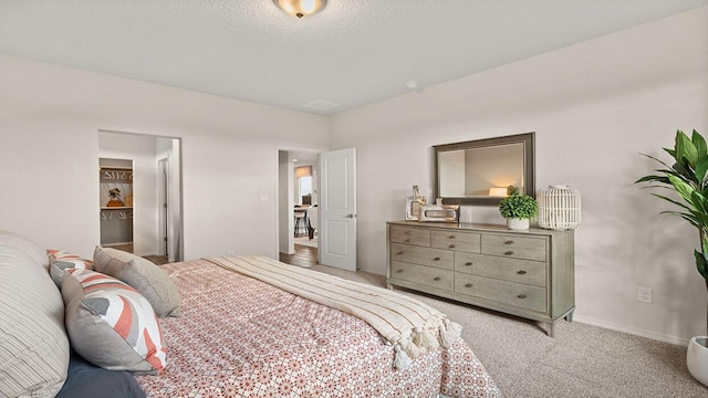 bedroom with baseboards, a textured ceiling, a walk in closet, and light colored carpet