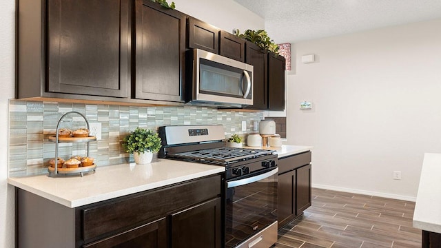 kitchen with dark brown cabinetry, wood tiled floor, backsplash, and appliances with stainless steel finishes