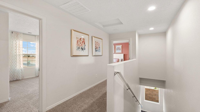 corridor featuring an upstairs landing, a textured ceiling, baseboards, visible vents, and carpet