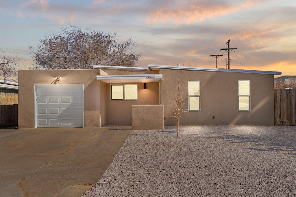 view of front of property with driveway, fence, an attached garage, and stucco siding