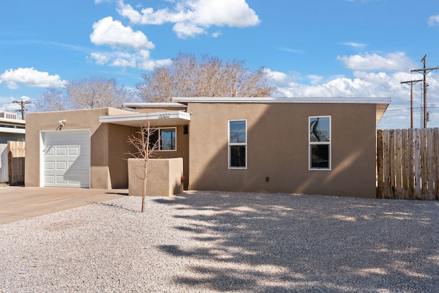 rear view of property with concrete driveway, an attached garage, fence, and stucco siding