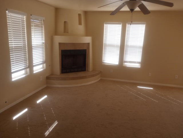 unfurnished living room featuring a ceiling fan, carpet flooring, a wealth of natural light, and a tile fireplace