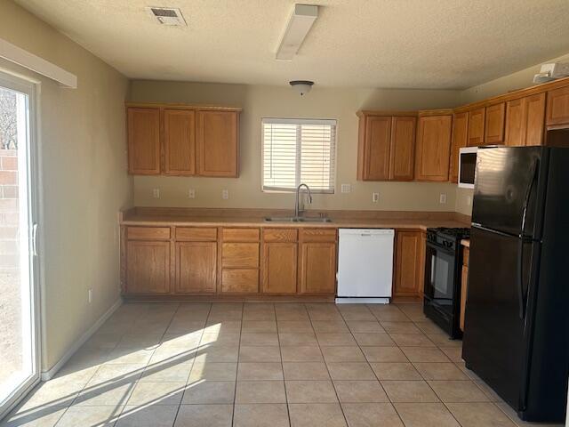 kitchen featuring light tile patterned floors, black appliances, a sink, and visible vents