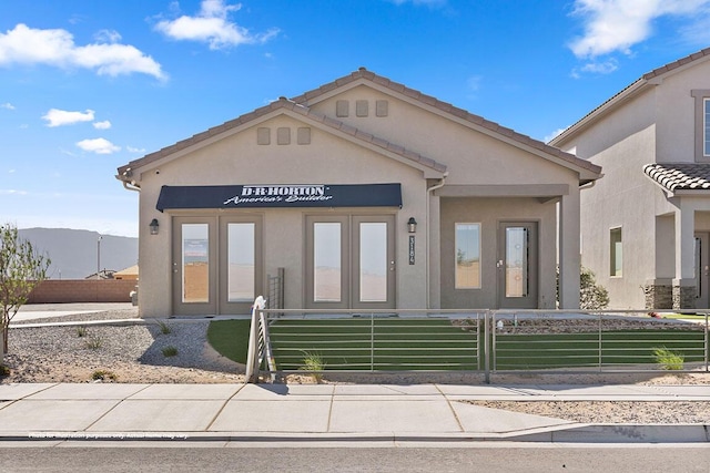 view of front of property featuring a fenced front yard, a mountain view, a tile roof, french doors, and stucco siding