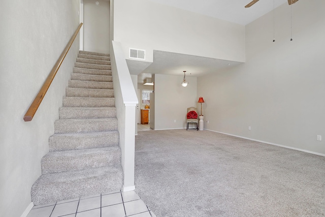 staircase with visible vents, a ceiling fan, tile patterned floors, a high ceiling, and carpet floors