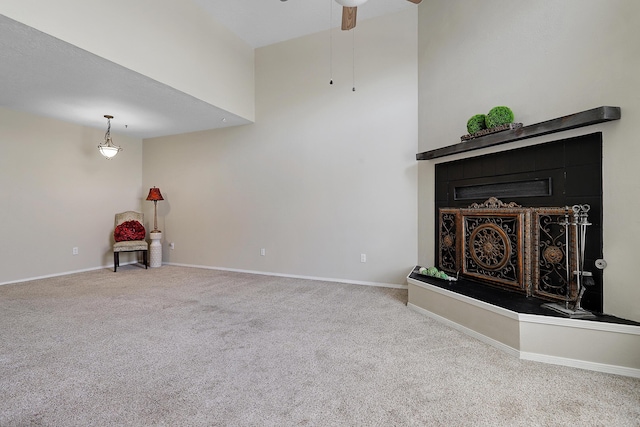 unfurnished living room featuring carpet floors, a fireplace with raised hearth, a high ceiling, a ceiling fan, and baseboards