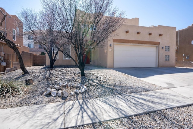 pueblo-style home with a garage, fence, driveway, and stucco siding