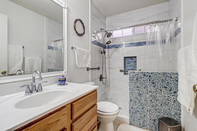 bathroom with a textured wall, vanity, a tile shower, and toilet