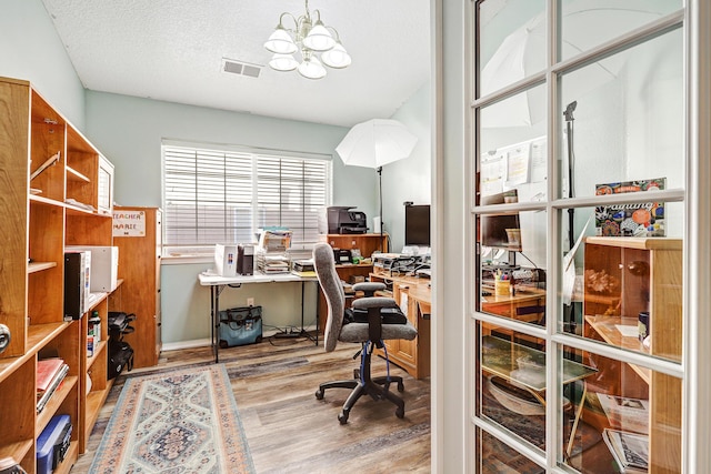 office space with a textured ceiling, wood finished floors, visible vents, and a chandelier