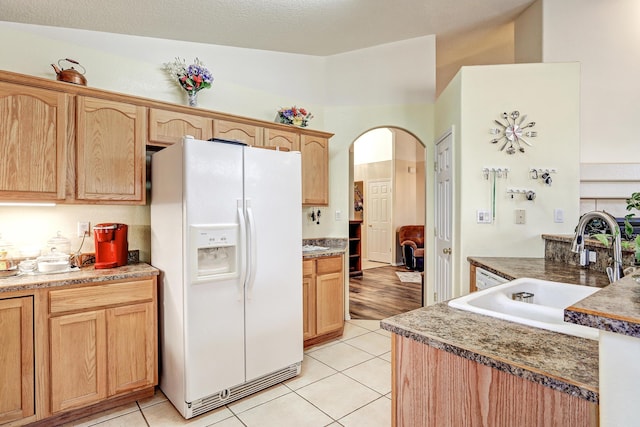 kitchen with light tile patterned floors, white refrigerator with ice dispenser, arched walkways, and a sink