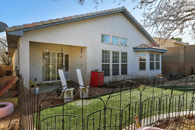 back of property featuring fence, a tile roof, a yard, stucco siding, and a patio area