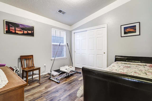 bedroom with visible vents, wood finished floors, vaulted ceiling, a textured ceiling, and a closet