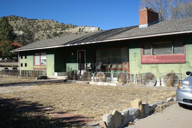 rear view of house featuring a chimney, concrete block siding, and roof with shingles