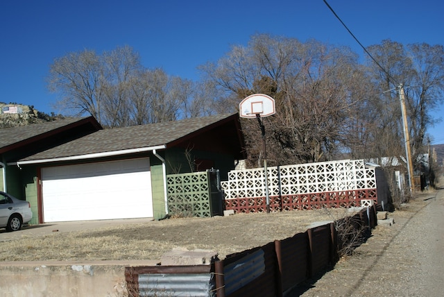 view of side of home featuring a shingled roof, fence, and concrete block siding