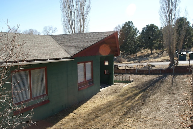 view of side of property featuring fence and roof with shingles