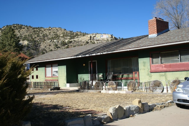 back of house featuring roof with shingles, a chimney, and concrete block siding