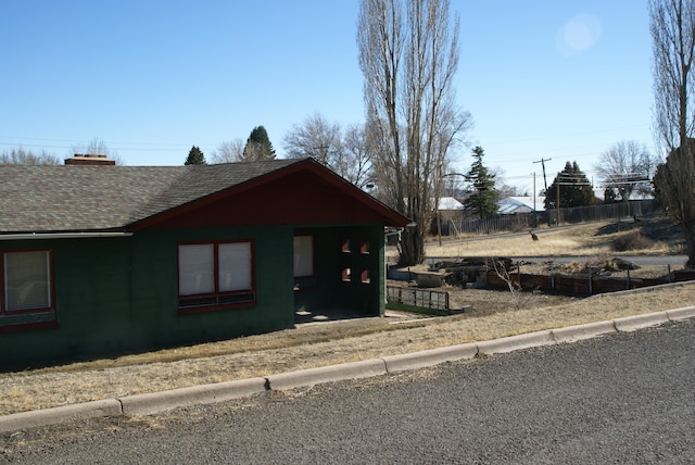 view of home's exterior with roof with shingles, fence, and a chimney