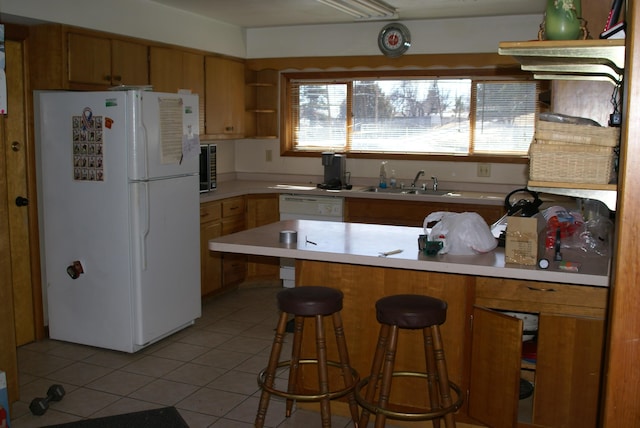 kitchen featuring dishwashing machine, freestanding refrigerator, a peninsula, light countertops, and a sink