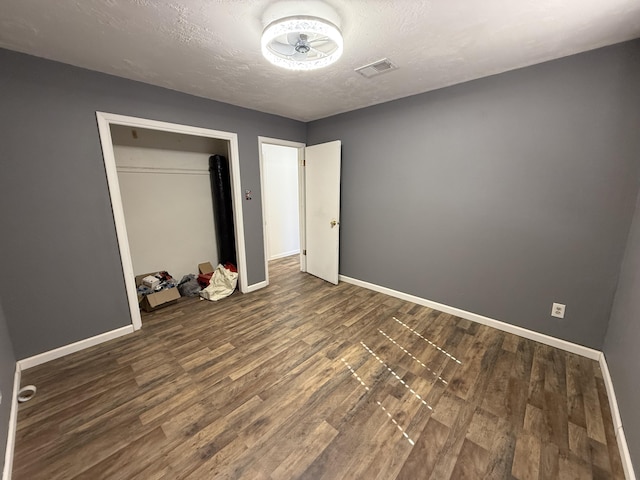 unfurnished bedroom with visible vents, dark wood finished floors, a textured ceiling, and baseboards