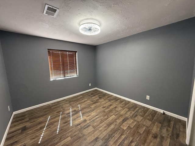 empty room with dark wood-style floors, visible vents, a textured ceiling, and baseboards