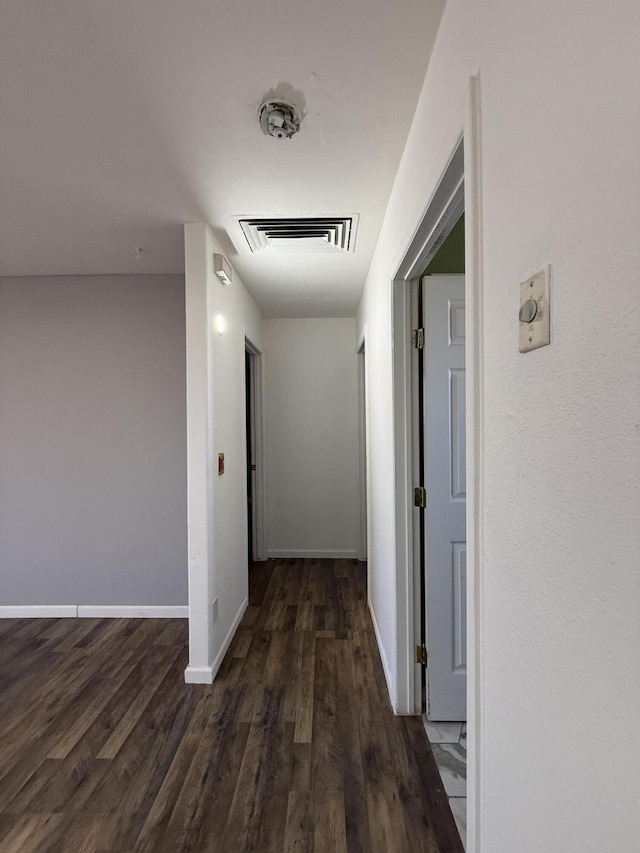 corridor featuring baseboards, visible vents, and dark wood-type flooring