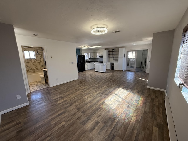 unfurnished living room with plenty of natural light, dark wood finished floors, visible vents, and baseboards