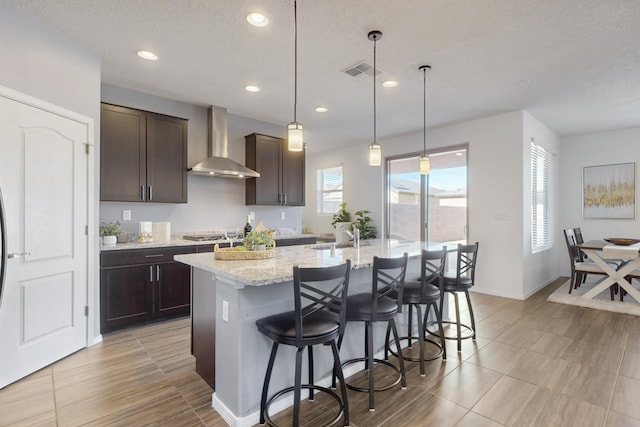 kitchen with wall chimney exhaust hood, visible vents, a kitchen breakfast bar, and dark brown cabinets