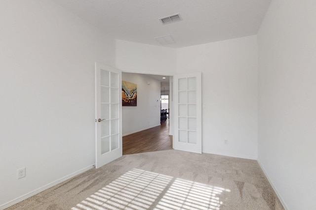 carpeted empty room with french doors, visible vents, and baseboards