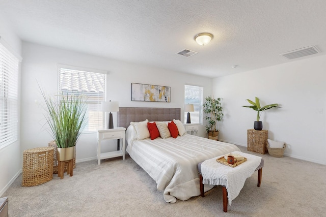 carpeted bedroom featuring a textured ceiling, multiple windows, and visible vents