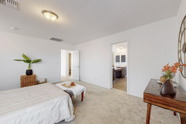 bedroom featuring light colored carpet, ensuite bath, visible vents, and a textured ceiling