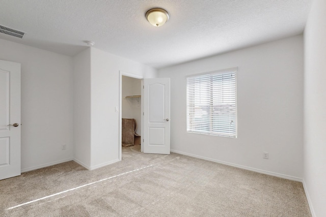 unfurnished bedroom with carpet floors, a walk in closet, visible vents, a textured ceiling, and baseboards