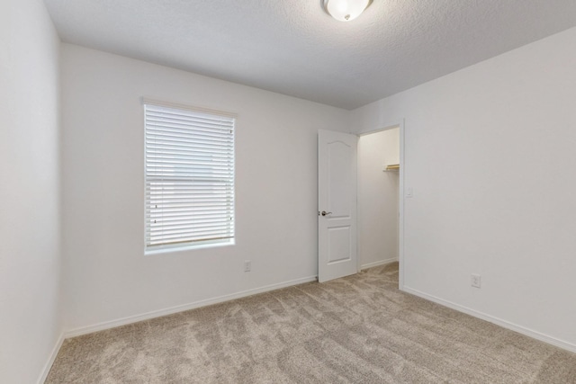 unfurnished room with a textured ceiling, baseboards, and light colored carpet