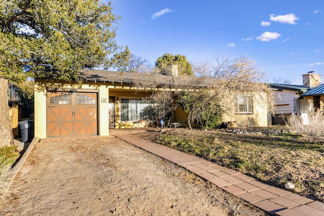 single story home featuring stucco siding, driveway, a chimney, and a garage