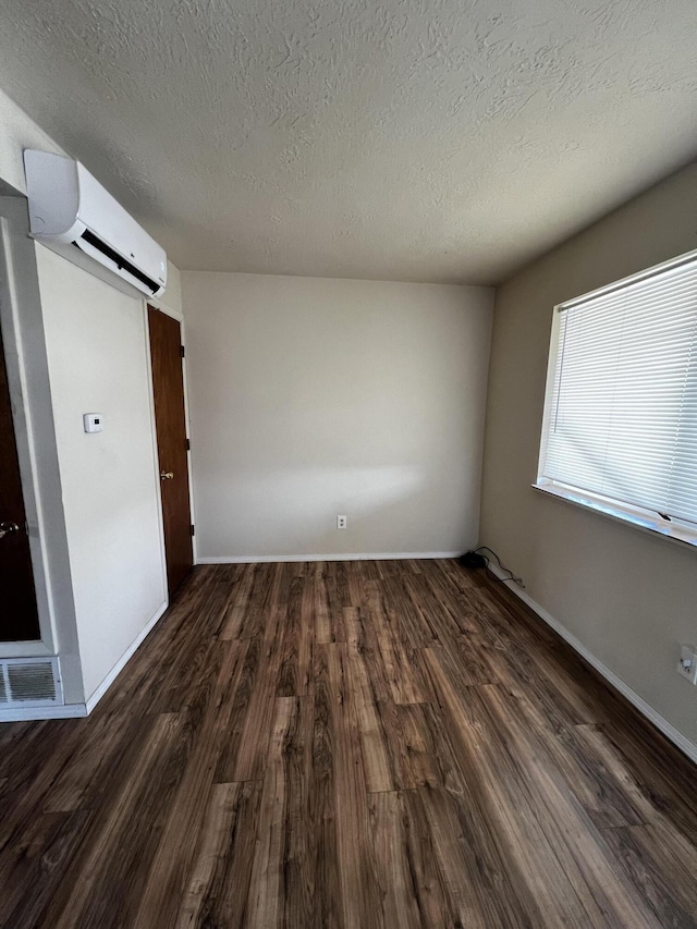 spare room with a textured ceiling, baseboards, wood finished floors, and a wall mounted AC