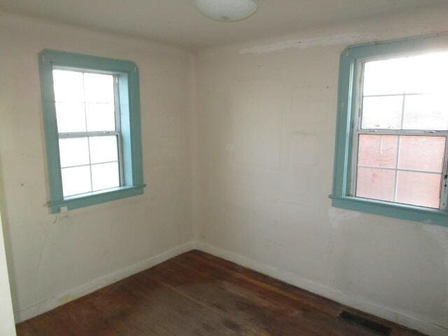 unfurnished room with dark wood-style flooring, visible vents, and baseboards