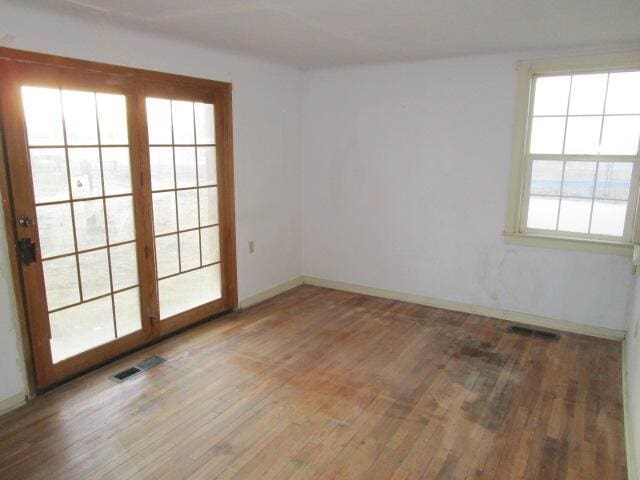 empty room with wood finished floors, visible vents, and baseboards