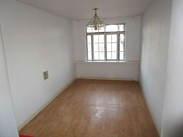 unfurnished room featuring wood finished floors, visible vents, and a notable chandelier