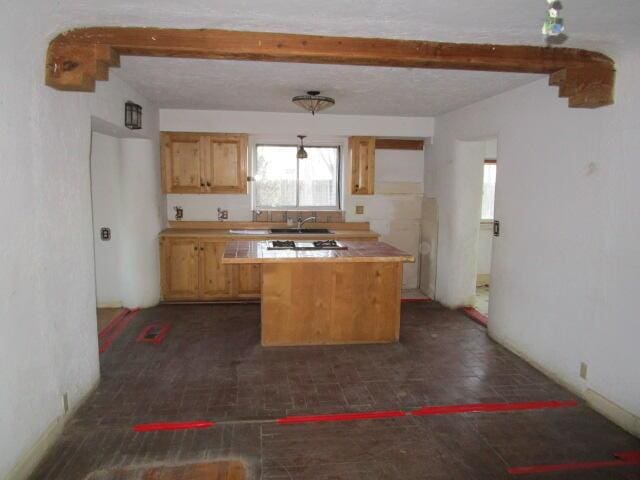 kitchen with a sink, light countertops, beamed ceiling, and light brown cabinetry