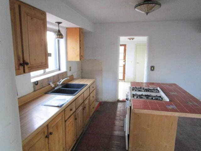 kitchen featuring tile counters, pendant lighting, a sink, and gas range gas stove