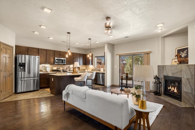 living area with a textured ceiling, light wood finished floors, a tiled fireplace, and baseboards