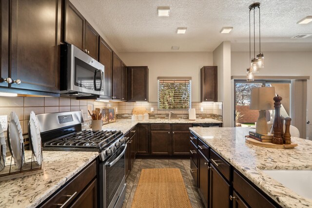 kitchen with stainless steel appliances, light stone countertops, visible vents, and dark brown cabinetry