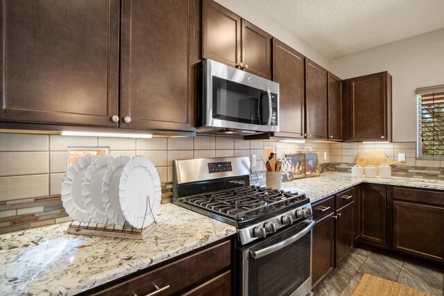 kitchen featuring dark brown cabinets, appliances with stainless steel finishes, backsplash, and light stone counters