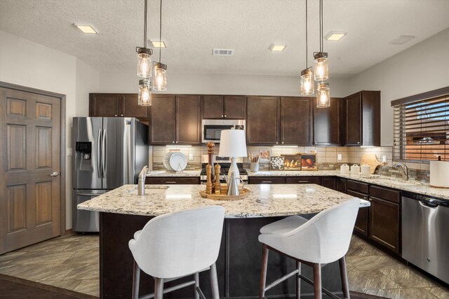 kitchen featuring a kitchen island, a sink, visible vents, dark brown cabinets, and appliances with stainless steel finishes